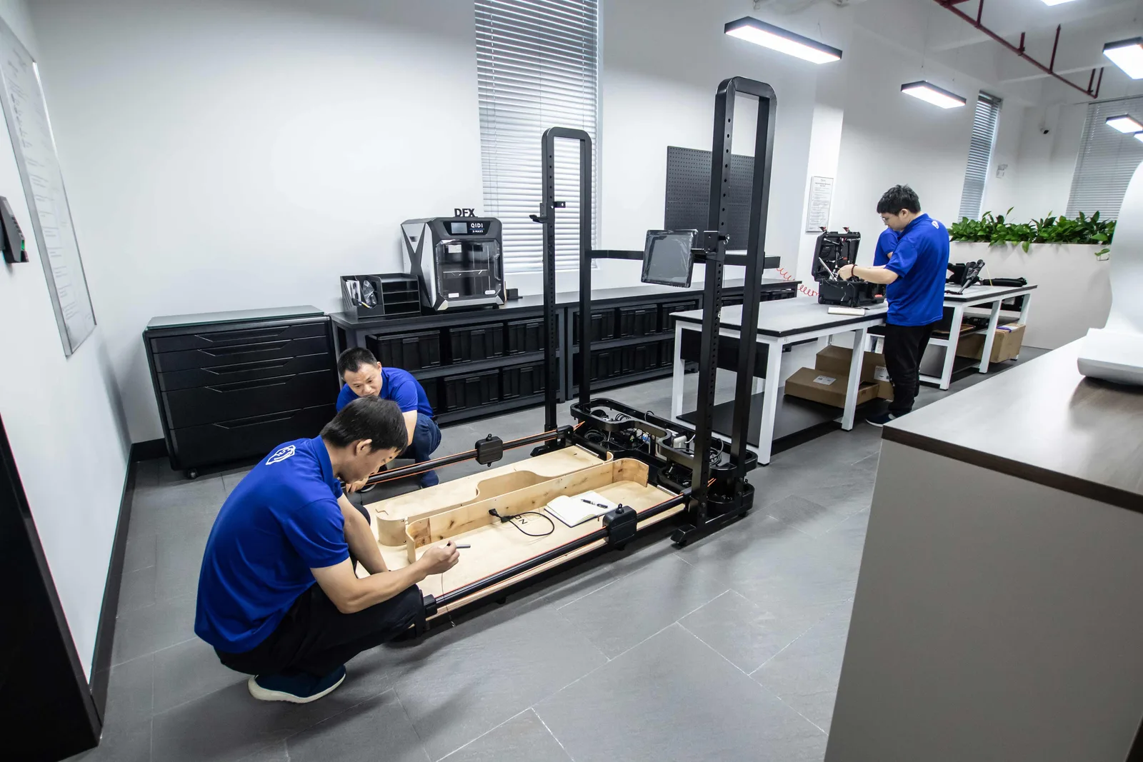Two engineers building a prototype frame on a jig in the DFX lab, with 3D printers along the back wall