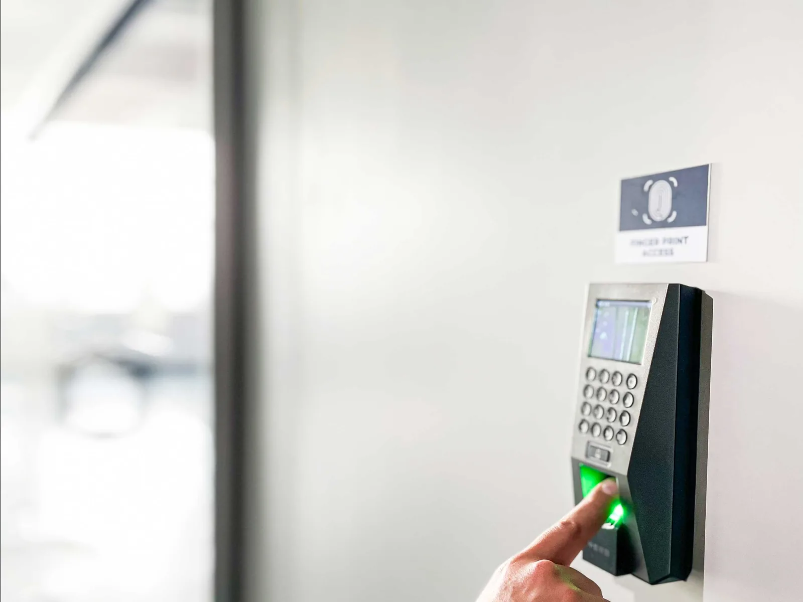 A hand pressing a fingerprint access reader on a white wall at Shield Works