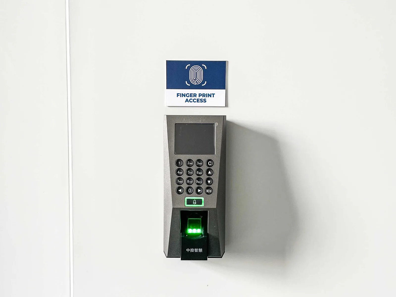 A fingerprint access reader mounted on a plain white wall inside the Shield Works facility