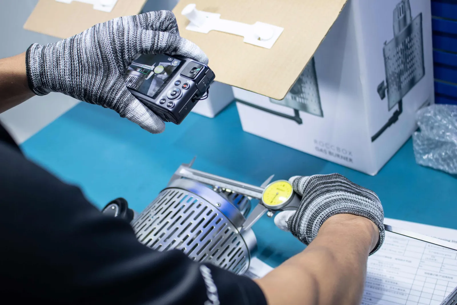 Gloved hands checking a component with a dial gauge and photographing the reading for the inspection record