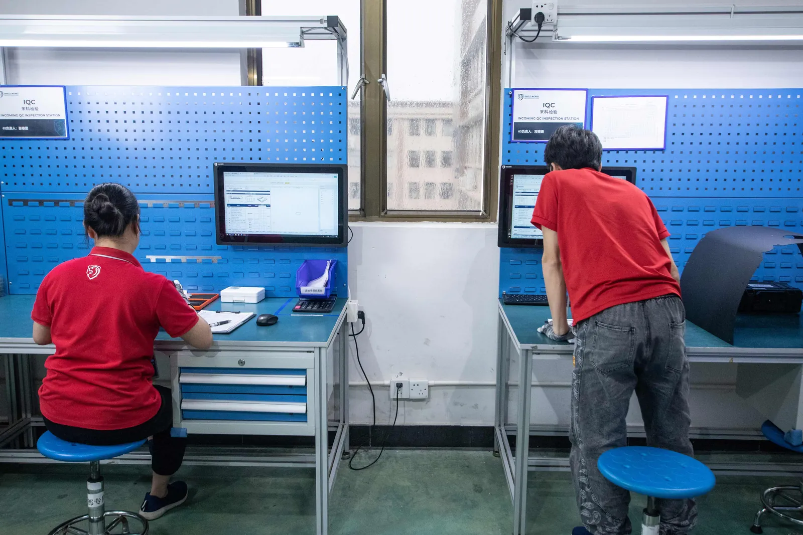 Inspectors at the incoming quality control stations, working at pegboard benches with monitors