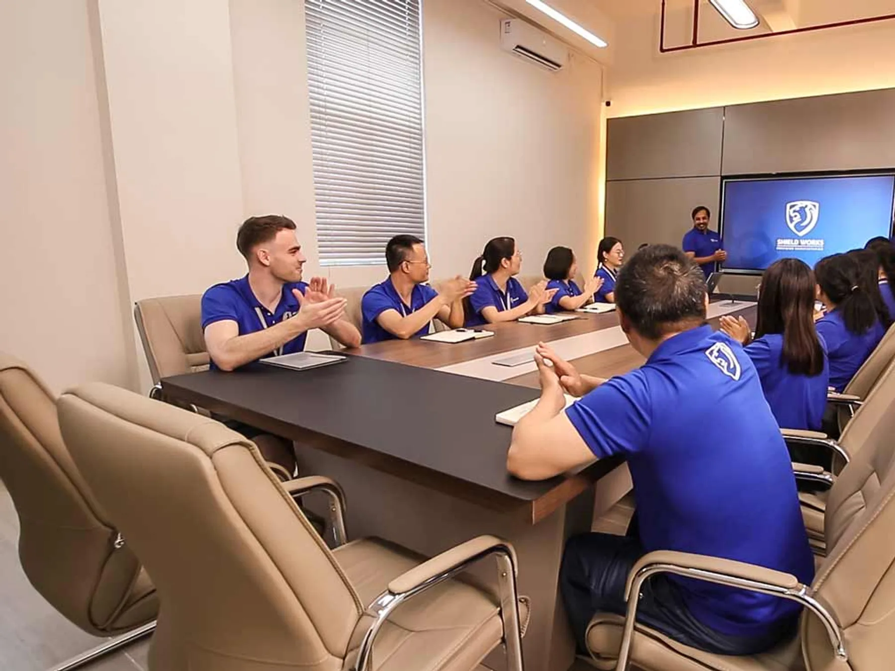 Shield Works team applauding around the boardroom table during a project review in Zhuhai