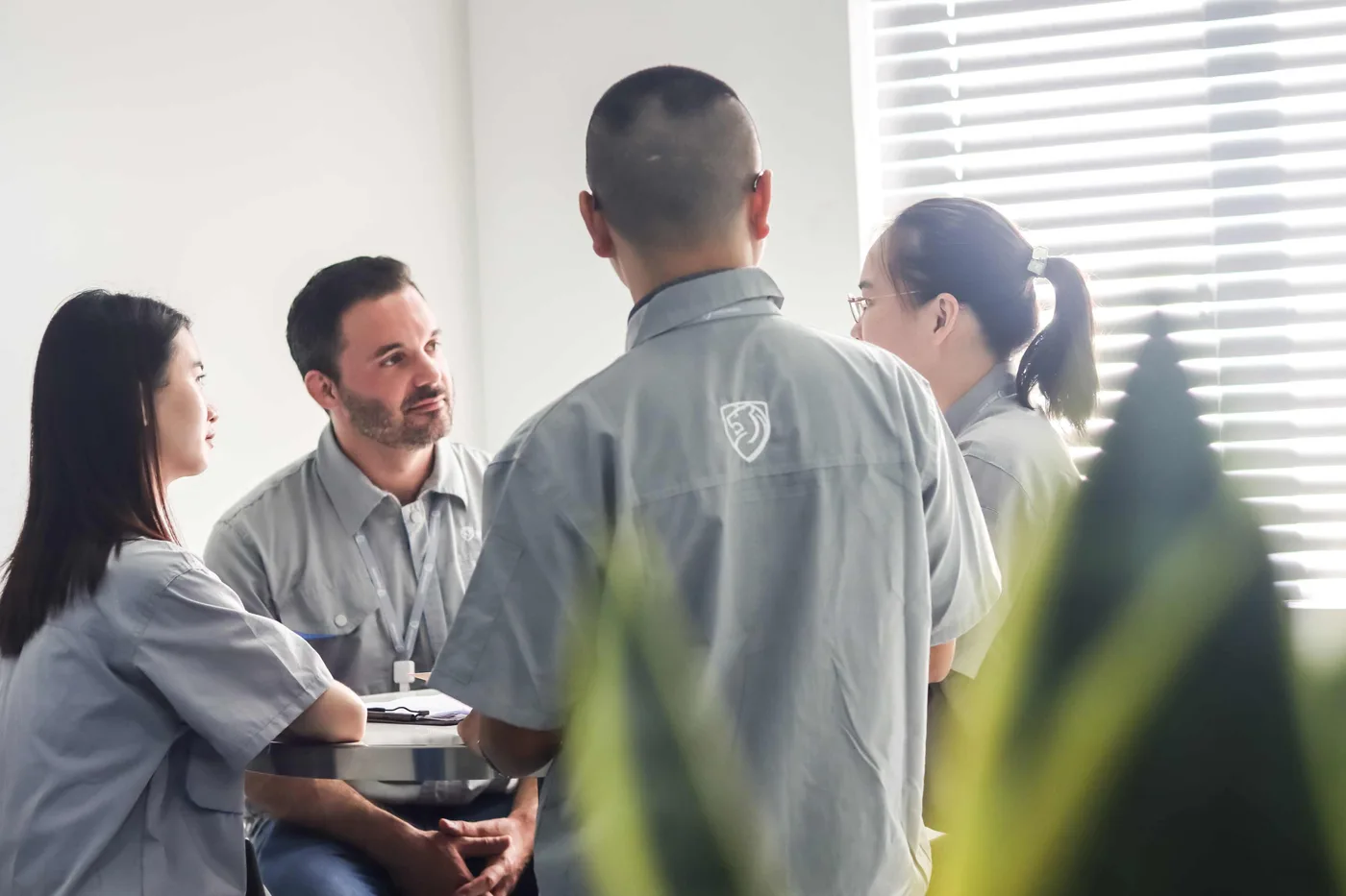 Western and Chinese Shield Works team members in a small in-person meeting wearing grey SW polo shirts