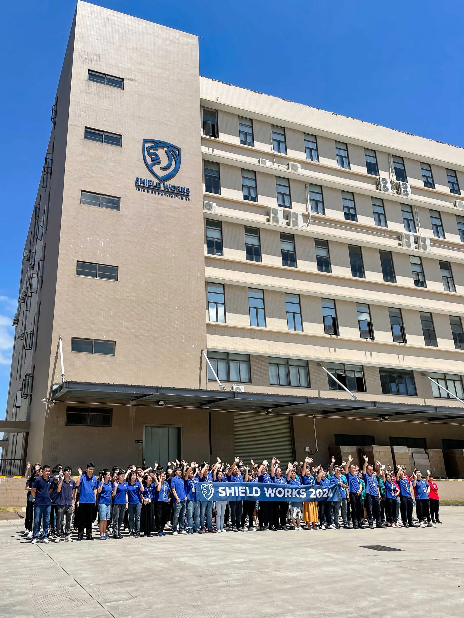 The full Shield Works team photographed in front of the Zhuhai facility holding a SHIELD WORKS banner